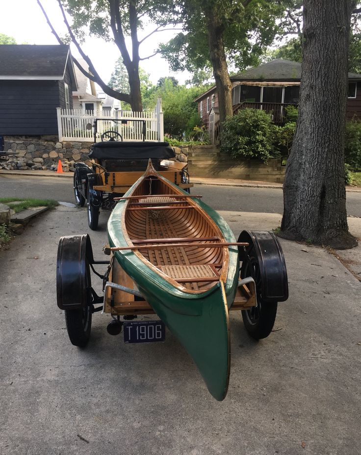 a green and brown boat sitting on top of a street next to a tree in front of a house