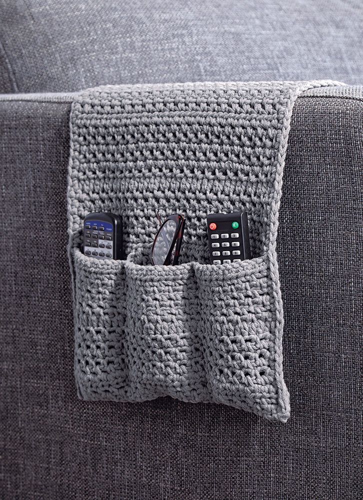 a crocheted pocket holds four remotes on the arm of a gray couch