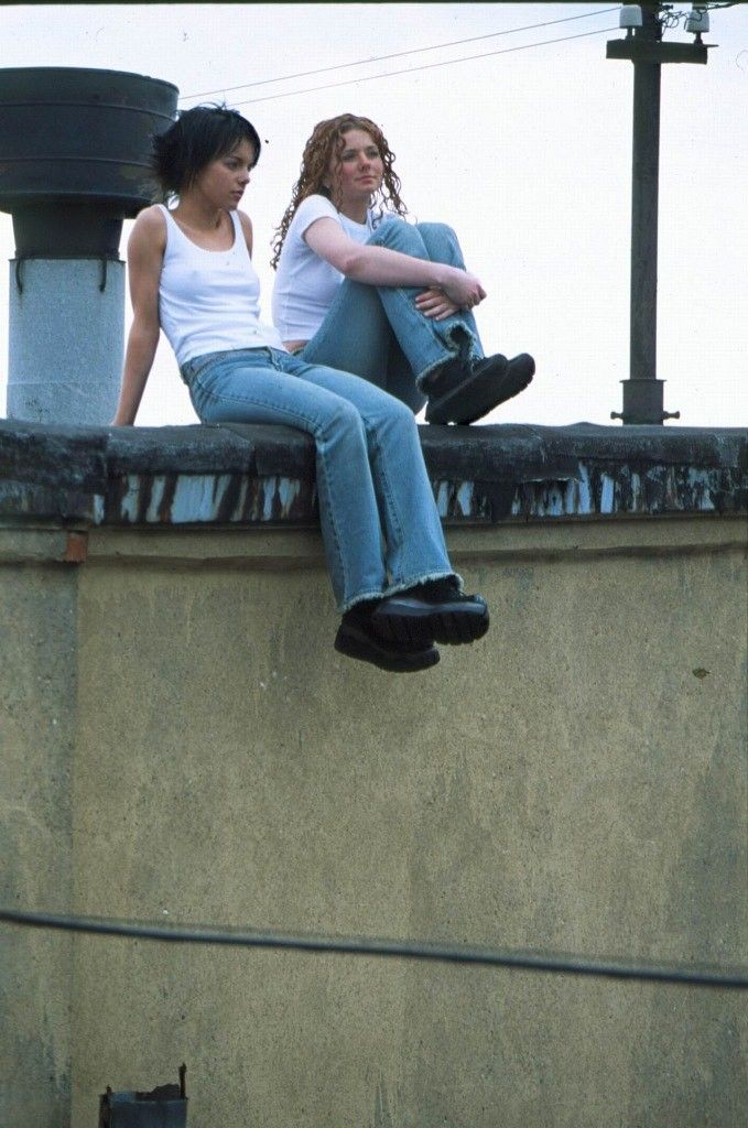 two women sitting on top of a cement wall