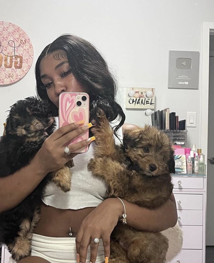 a woman taking a selfie while holding two small dogs in her lap and looking at her phone