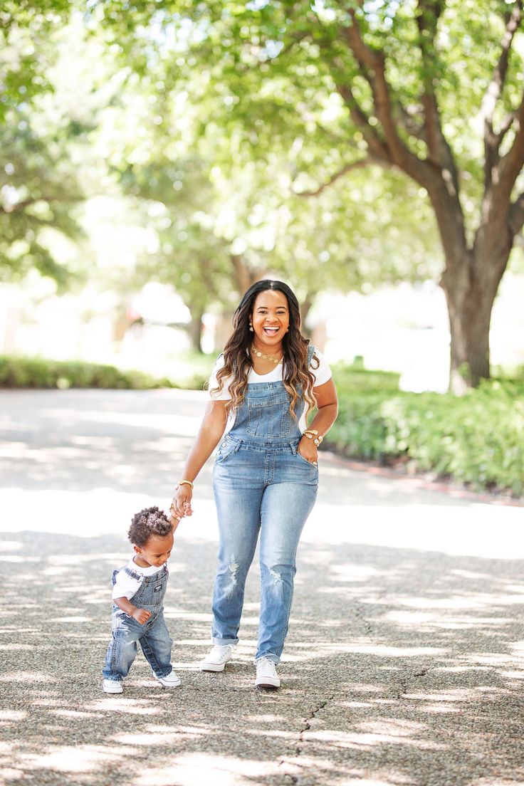 a woman holding the hand of a small child while walking down a street with trees in the background