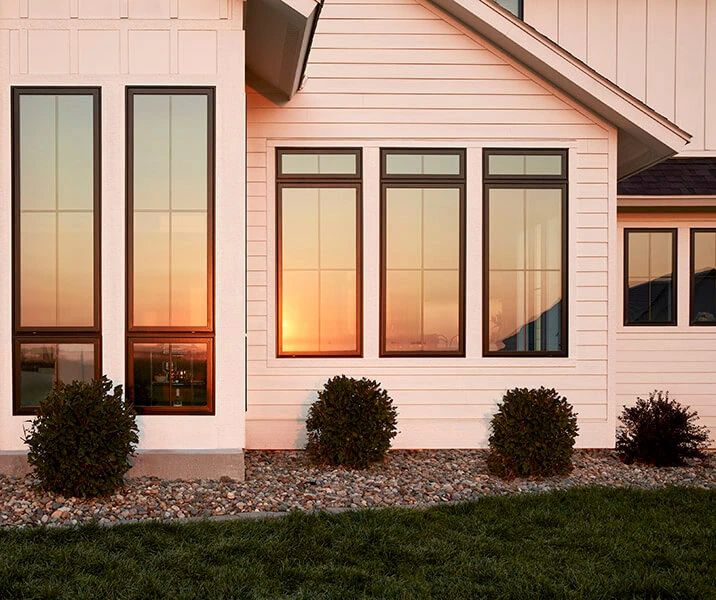 the sun is setting in front of a white house with black trim and three windows