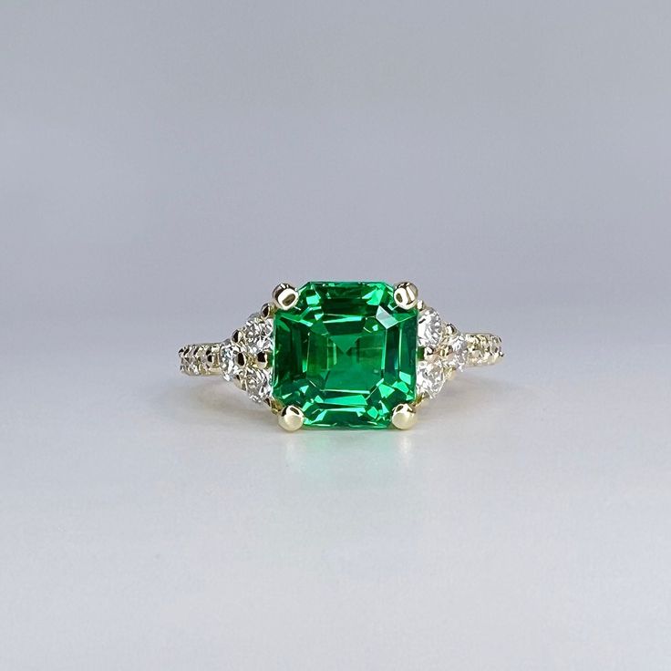 an emerald and diamond ring on a white surface