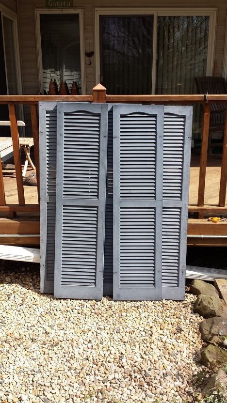 two open shutters sitting on top of a gravel covered ground next to a wooden deck