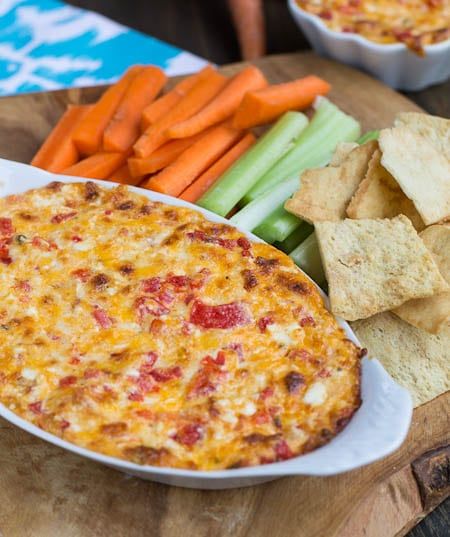 a bowl of dip, crackers and carrots on a cutting board