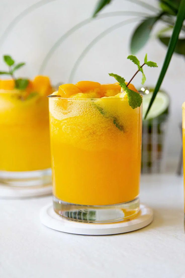 three glasses filled with orange juice and garnished with green leaves on the rim