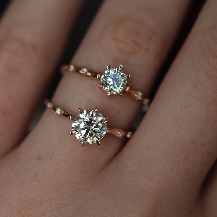 two gold rings with diamonds on them are sitting on someone's hand, one is wearing a diamond ring and the other has an engagement ring