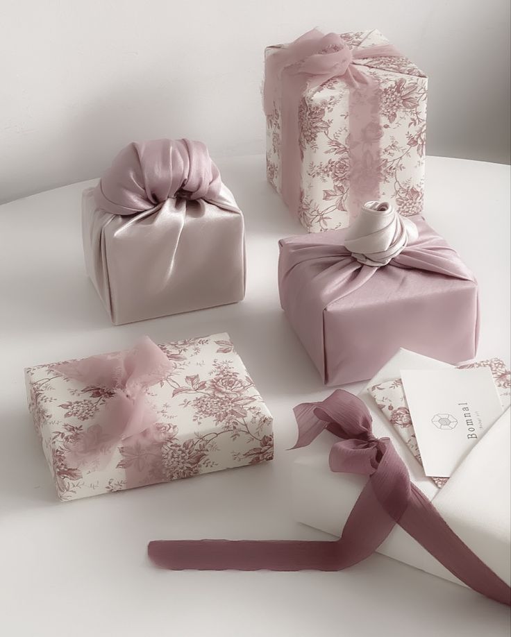 four wrapped gift boxes with pink ribbons and bows on white table cloth, all decorated in pastel tones