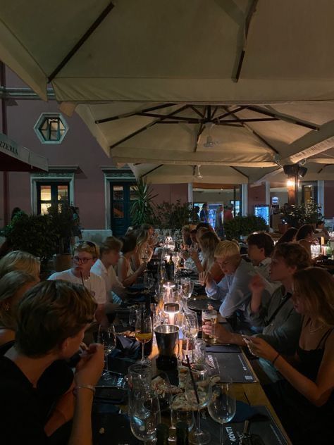 a group of people sitting at a long table with wine glasses on top of it