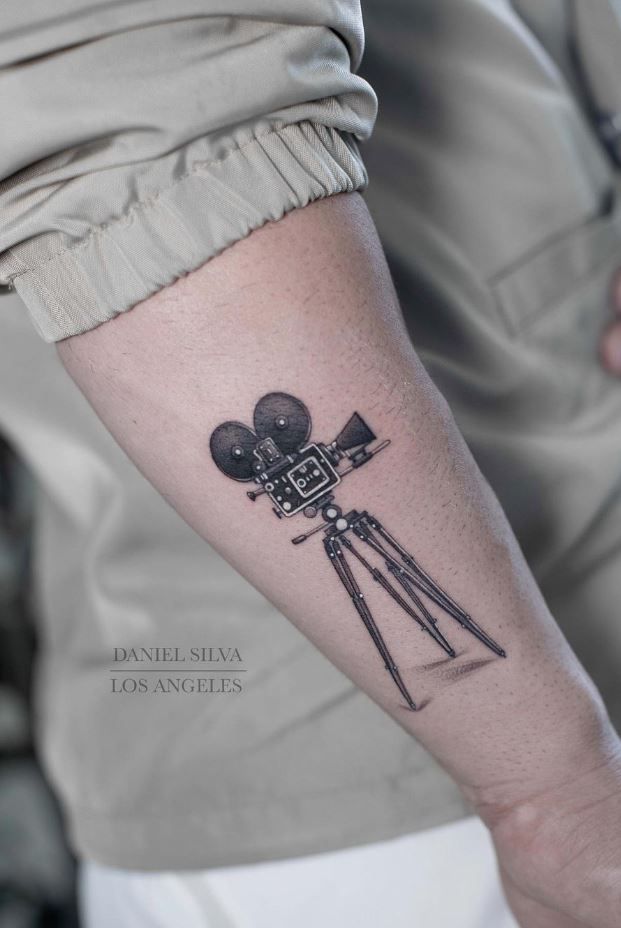 a man with a camera tattoo on his arm, holding a tripod and looking at the sky