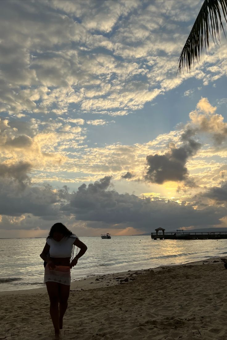 a woman standing on top of a sandy beach next to the ocean under a cloudy sky