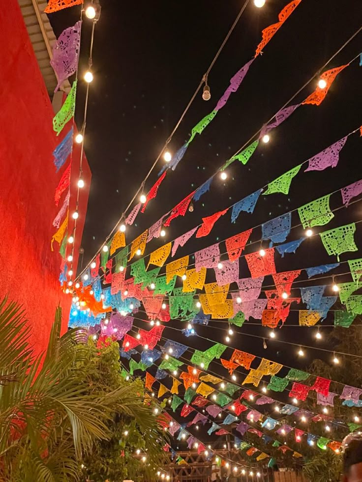 many colorful flags hanging from the ceiling in an open area with lights and palm trees