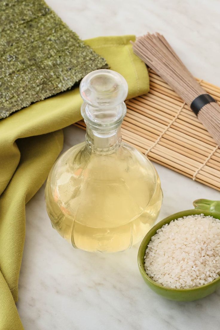 a bottle of white rice next to a green bowl and bamboo utensils on a table