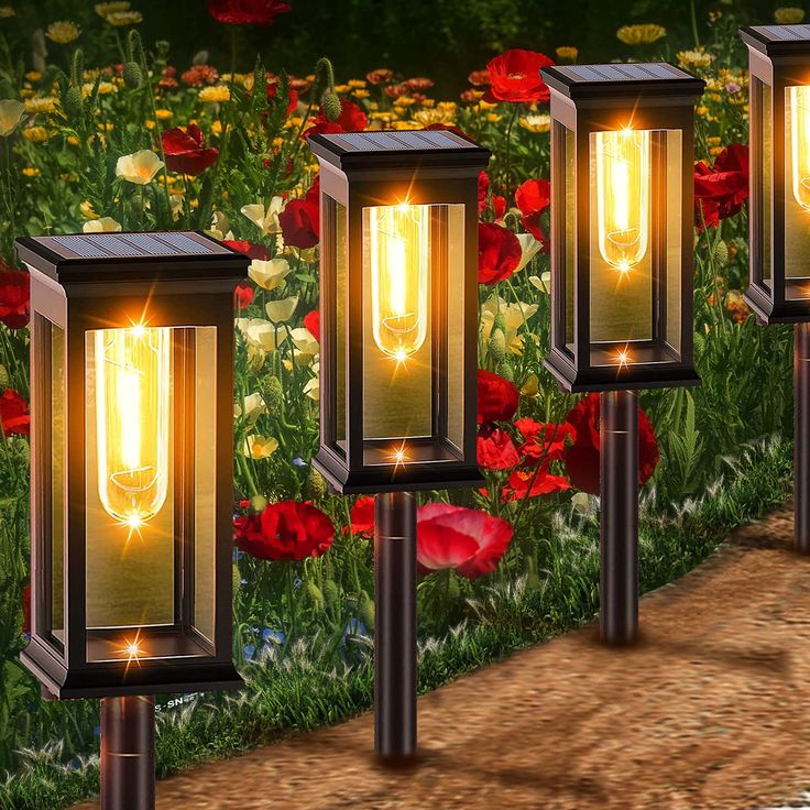 three solar powered garden lights in front of red flowers and green grass with one glowing