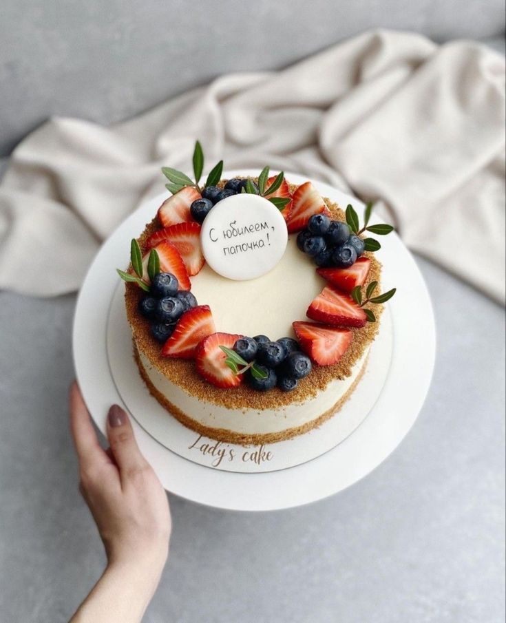 a cake with berries and blueberries on top is being held by a woman's hand