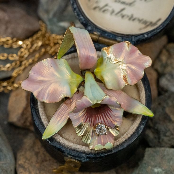 This gorgeous diamond flower pendant features an Iris flower that has been enameled in opalescent pink, green, and white enamels. The center of the flower is set with an Old Mine cut diamond accent. The pendant necklace is crafted in patinated 14k yellow gold and is a brooch conversion. It hangs on a 16" diamond cut cable chain. There is very minor enamel loss. Flower Shaped Enamel Jewelry For Wedding, Art Nouveau Rose Gold Jewelry As A Gift, Flower Shaped Enamel Wedding Jewelry, Enamel Flower Shaped Wedding Jewelry, Art Nouveau Rose Gold Jewelry As Gift, Art Nouveau Rose Gold Jewelry For Gift, Rose Gold Art Nouveau Jewelry For Gift, Victorian Pink Diamond Jewelry, Flower-shaped Enamel Jewelry For Wedding