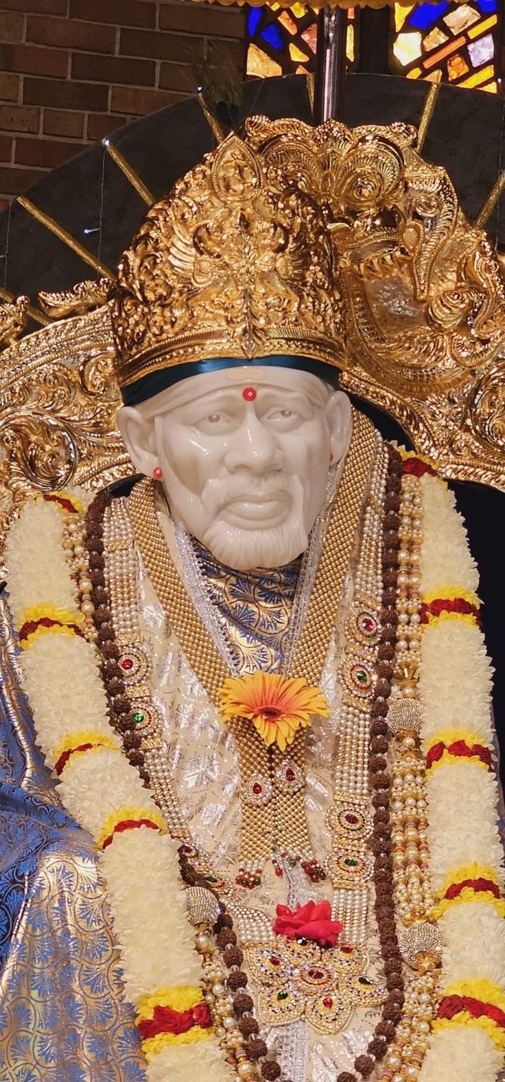 the statue is dressed in gold and white with beads on it's head, wearing a crown