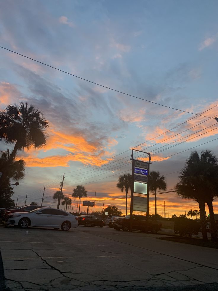 a parking lot filled with lots of parked cars under a cloudy blue and orange sky