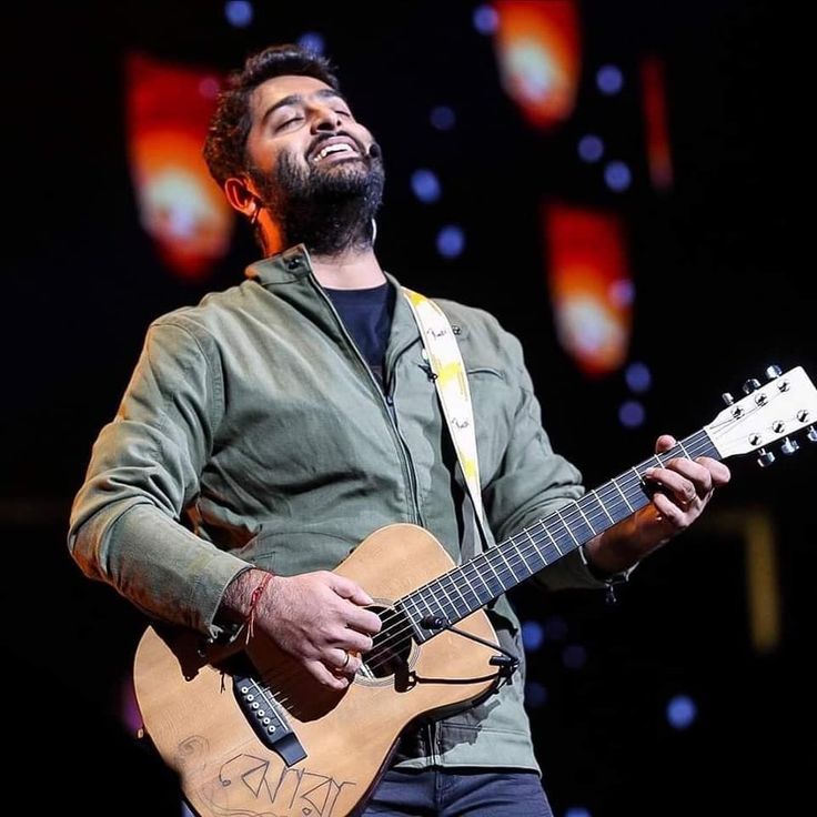 a man with a beard playing an acoustic guitar at a concert in front of bright lights