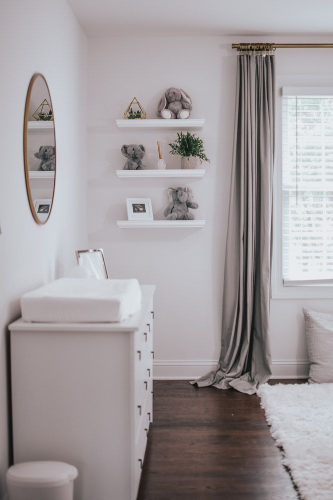 a baby's room with white walls and wooden floors, shelves on the wall