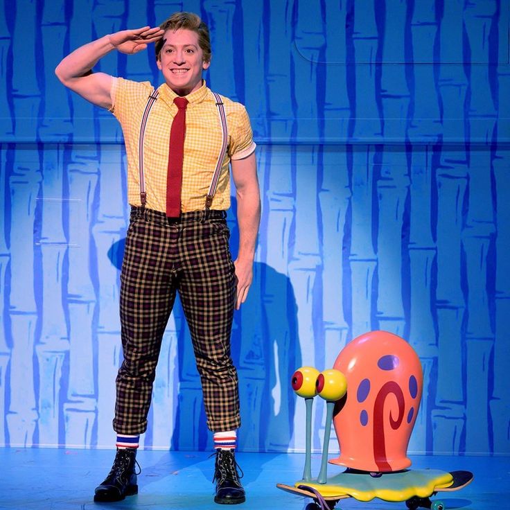 a man standing next to a skateboard on top of a blue stage background with a giant snail