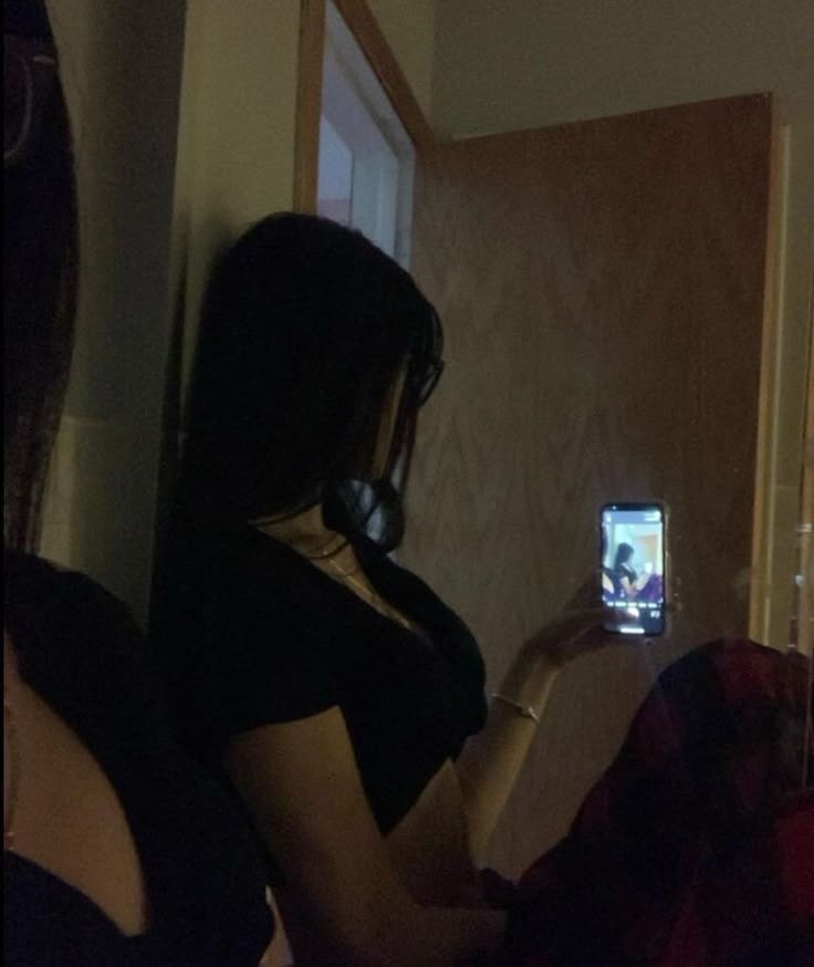 a woman taking a selfie with her cell phone in the dark, while sitting on a couch