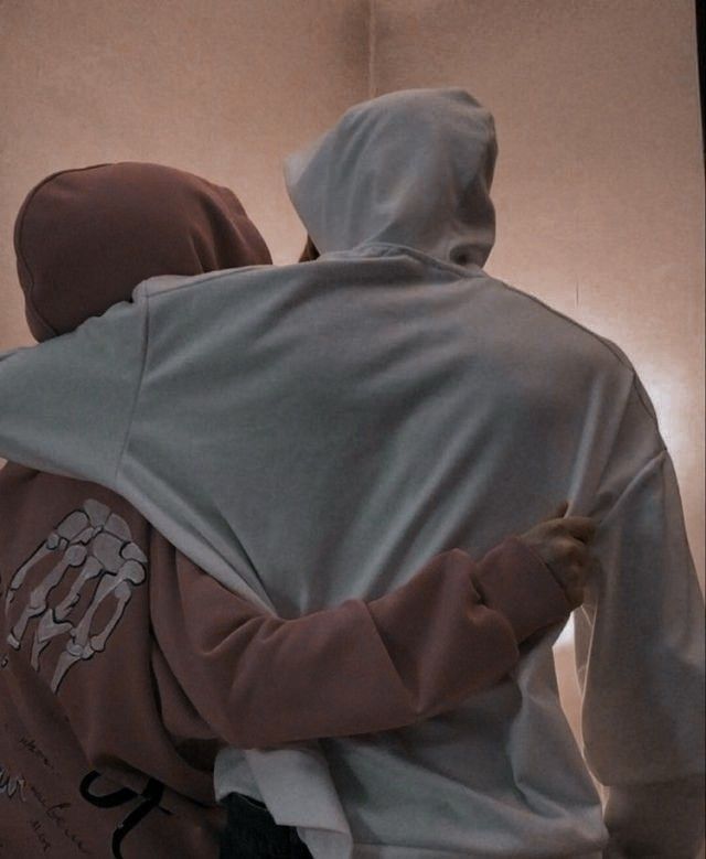 two people in hooded sweatshirts hugging each other with their backs to the camera,