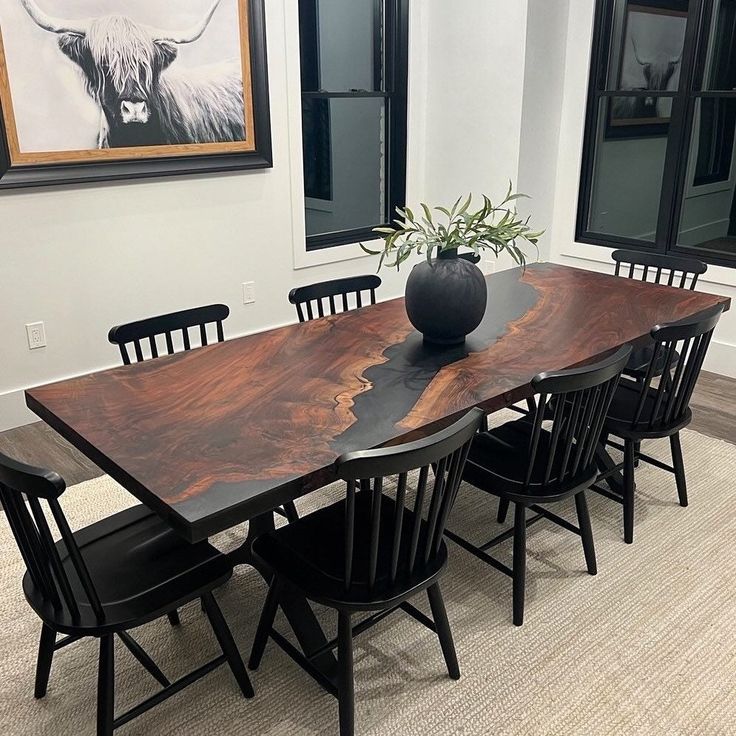 a wooden table with black chairs and a vase on top of it in a room