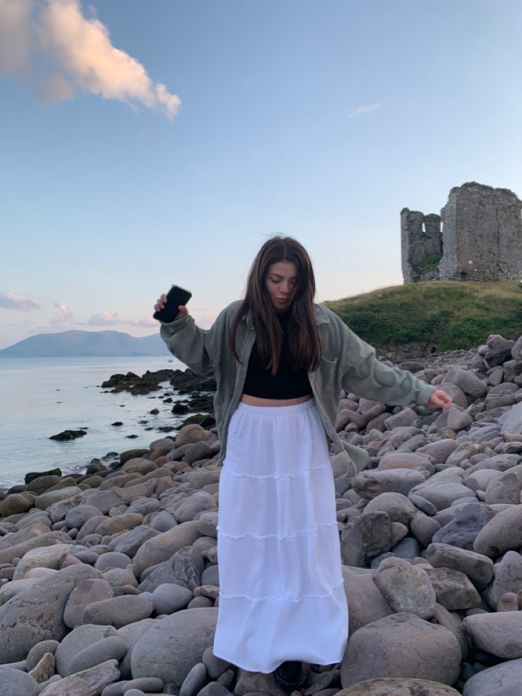 a woman standing on rocks near the ocean with her arms outstretched in front of her