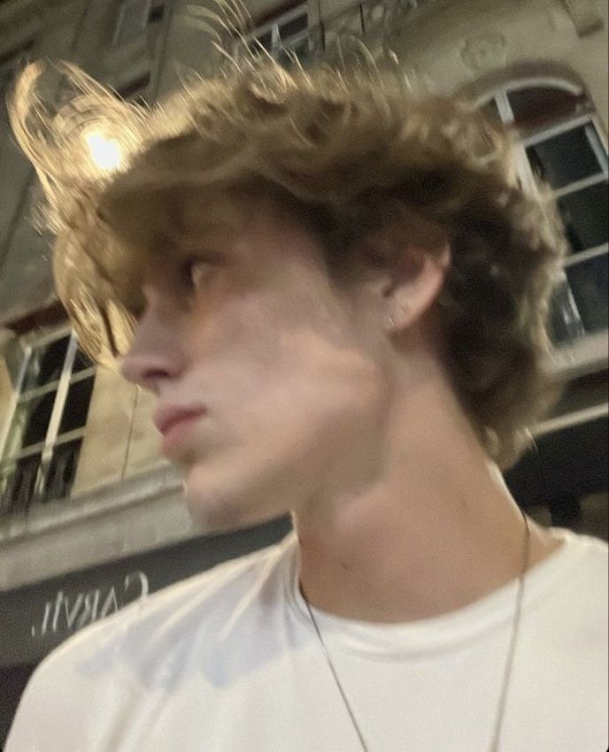 a close up of a person wearing a necklace and a white t - shirt in front of a building