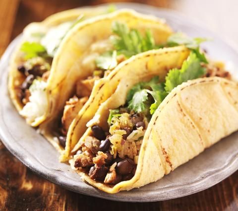 three tacos on a plate with cilantro, black beans and other toppings