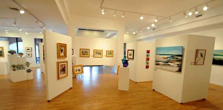 an art gallery with paintings on the walls and wooden flooring in front of them