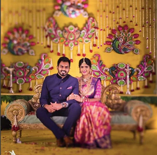 a man and woman sitting on a bench in front of a yellow wall with colorful decorations