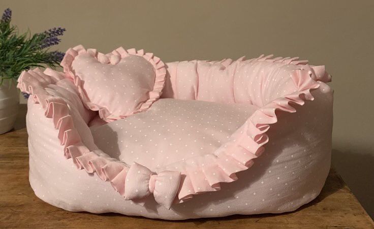 a pink dog bed with ruffles on it and a potted plant in the background