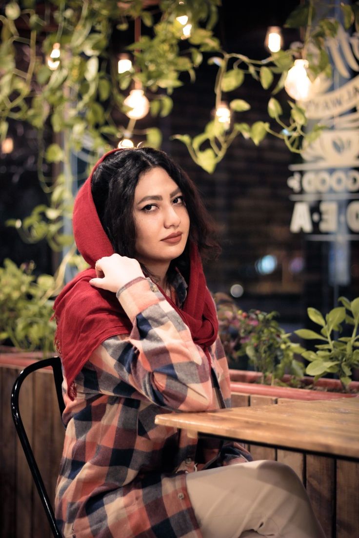 a woman sitting at a table wearing a red hoodie and holding her hand up to her ear