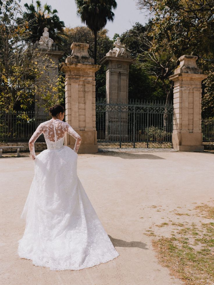 a woman in a white wedding dress is standing near an iron gate and looking at the ground