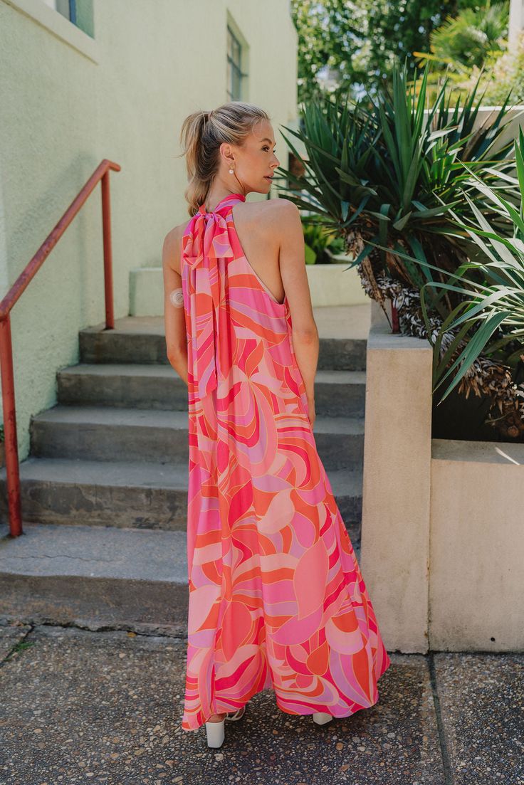 The Josephine Multicolor Printed Halter Maxi Dress is a vibrant and eye-catching garment that exudes summer elegance and playful charm. Its bold color palette of red-orange, pink, and purple creates a stunning visual impact, reminiscent of a tropical sunset or a vivid summer garden in full bloom. Crafted from lightweight fabric, this maxi dress flows effortlessly with every step, offering both comfort and style for warm-weather occasions. The halter neckline of the Josephine dress adds a touch of sophistication while providing support and structure to the silhouette. Its sleeveless design allows for freedom of movement, making it perfect for outdoor events or beachside strolls. A geometric pattern adorns the fabric of the dress, adding depth and visual interest to the overall design. The p Coral Summer Beach Dress, Coral Beach Dress For Summer, Coral Dresses For Spring Vacation, Pink Halter Neck Maxi Dress For Summer, Pink Sleeveless Dress For Beach Party, Spring Coral Vacation Dresses, Coral Spring Vacation Dresses, Spring Vacation Coral Dresses, Pink Sleeveless Beach Dress For Spring