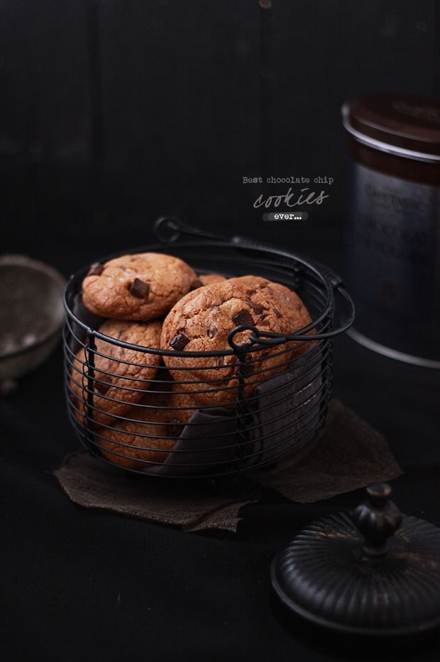 chocolate chip cookies in a wire basket on top of a table next to a cookie tin