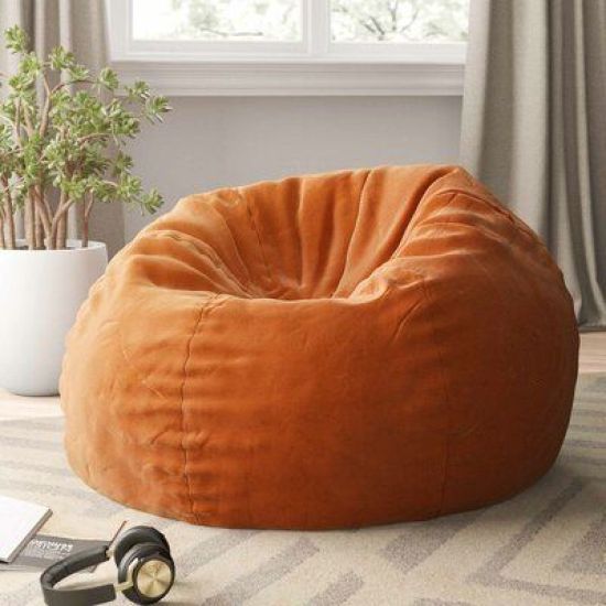 an orange bean bag chair sitting on top of a rug next to a potted plant