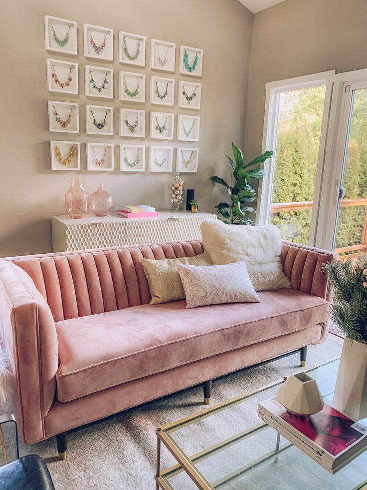 a living room with pink velvet couches and pictures on the wall above them,