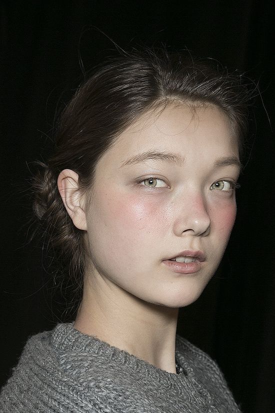 a young woman with freckled hair and green eyes looks at the camera while wearing a gray sweater