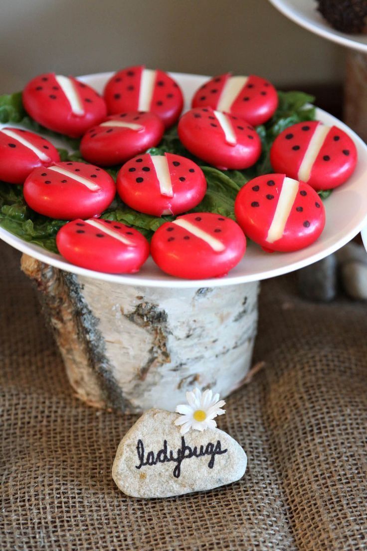 red ladybugs are sitting on top of a white cake plate with flowers in it