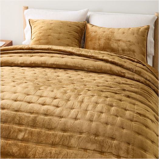 a bed with gold comforter and pillows on it in a bedroom setting that has white walls