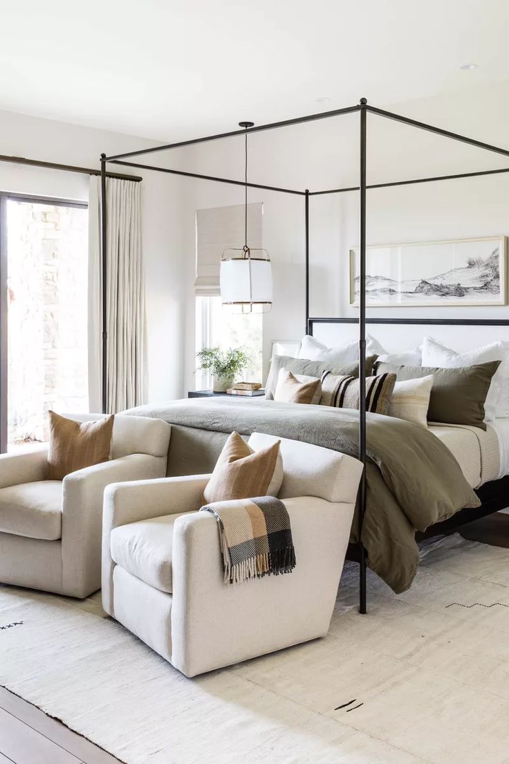 a bedroom with four poster bed, white couch and beige chair in front of it