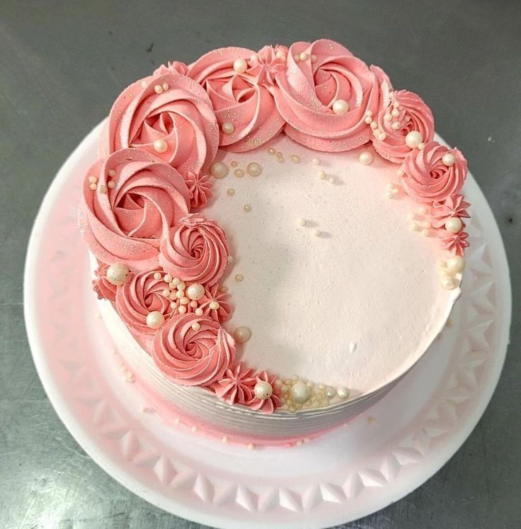 a cake with pink frosting and roses on top is sitting on a white plate