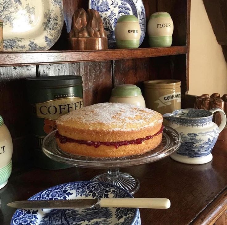 a cake sitting on top of a wooden table next to cups and saucers with spoons