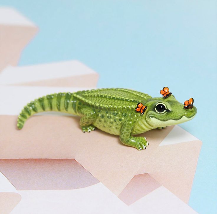 a small green toy alligator sitting on top of a pink and blue surface with geometric shapes in the background