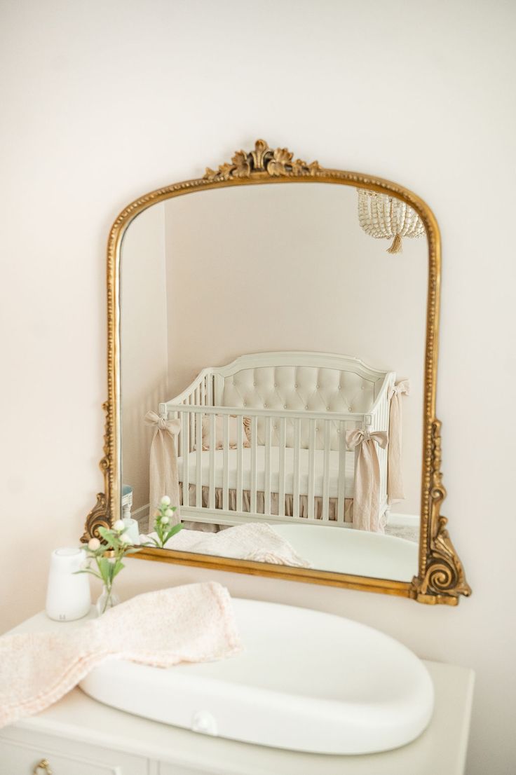 a white crib with a gold framed mirror above it and a baby crib in the background