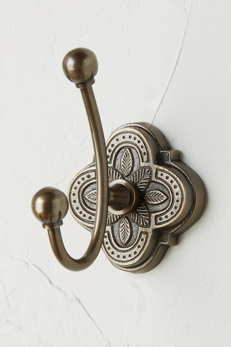 an ornately designed metal hook on a white wall with a flower design in the center