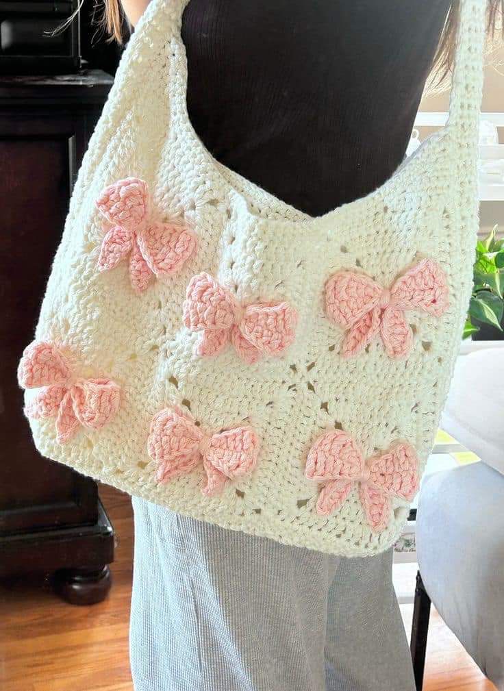 a crocheted bag with pink bows on the front and bottom, hanging from a mannequin's torso